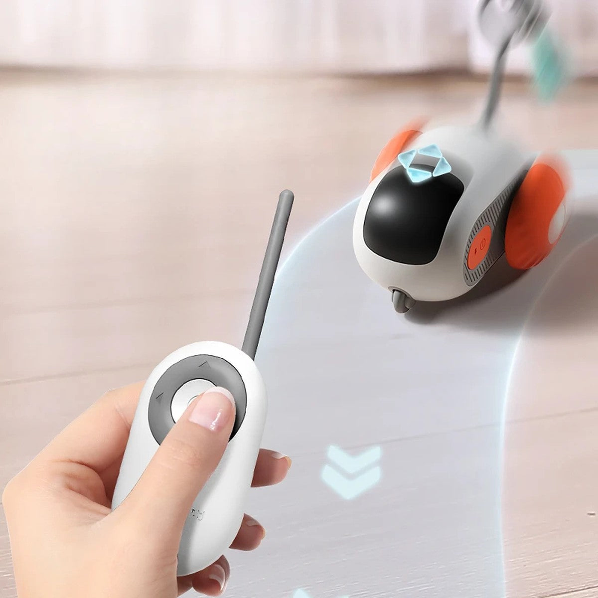 Hand holding the Pouncebot remote while the car drives across a wooden floor